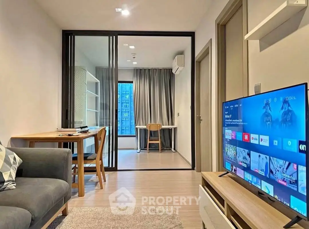 Modern living room with sleek furniture and glass partition leading to a study area.