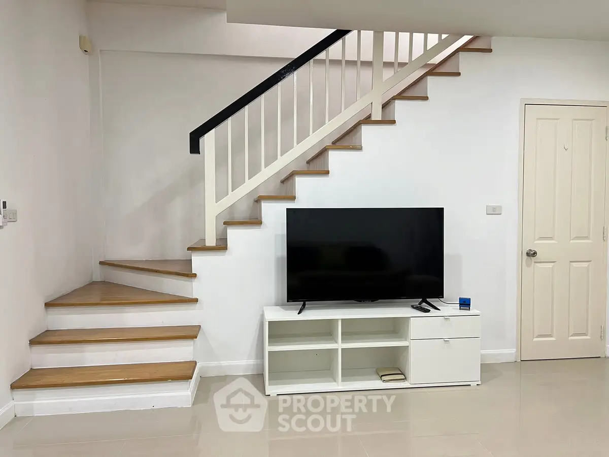 Modern living room with sleek staircase and large flat-screen TV, perfect for contemporary living.