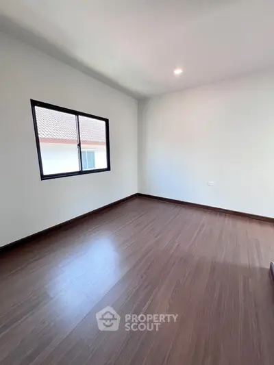 Spacious empty room with wooden flooring and natural light from window.