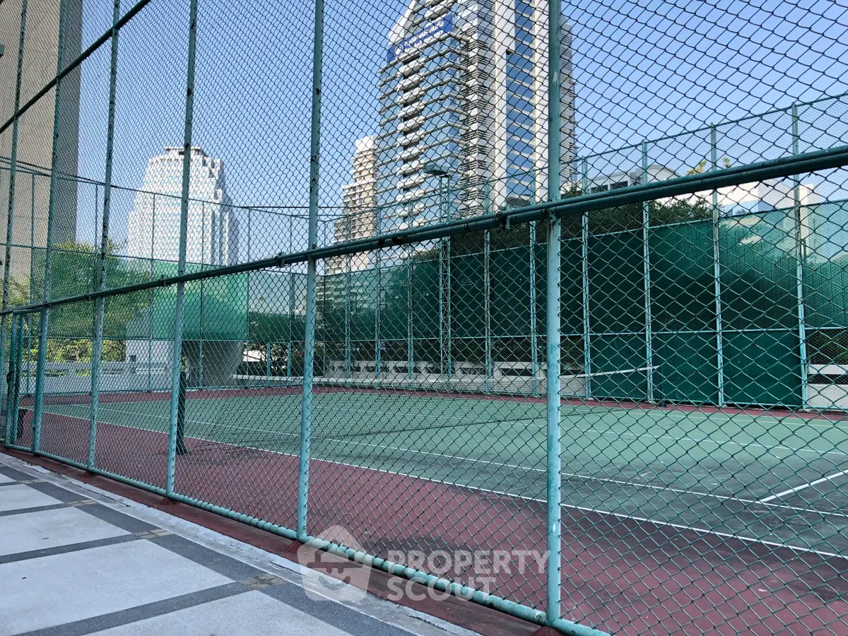 Spacious urban tennis court with high-rise buildings in the background, ideal for sports enthusiasts.