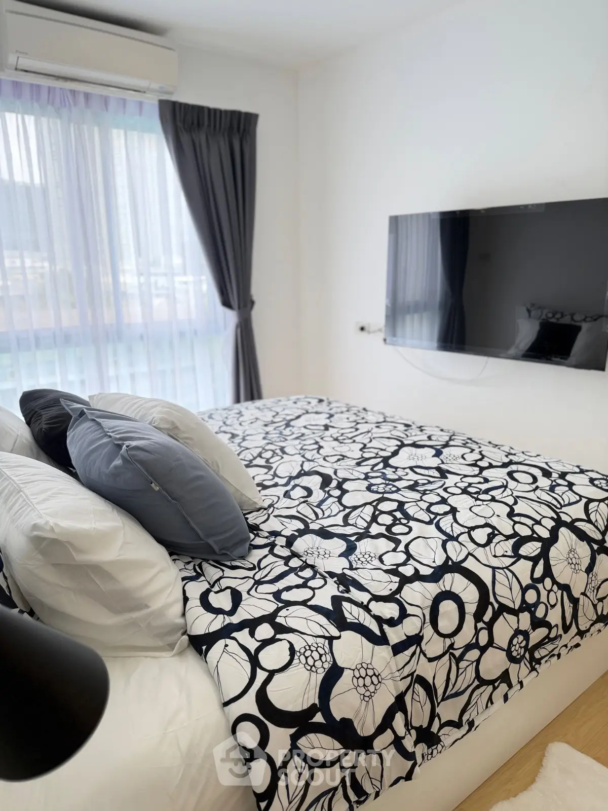 Cozy bedroom with modern decor and wall-mounted TV, featuring a large window with elegant curtains.