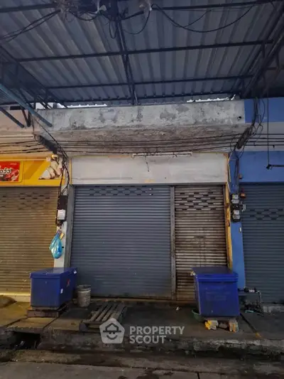Closed commercial storefront with metal shutters and overhead awning in urban setting.