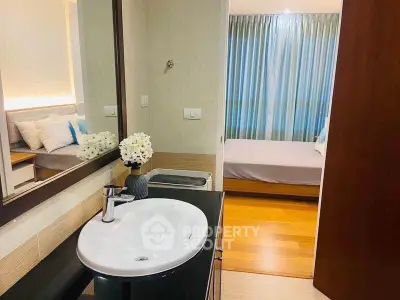 Modern bathroom with sleek sink and view into cozy bedroom with wooden flooring.
