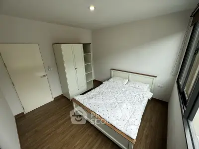 Spacious bedroom with wooden flooring and large window for natural light.
