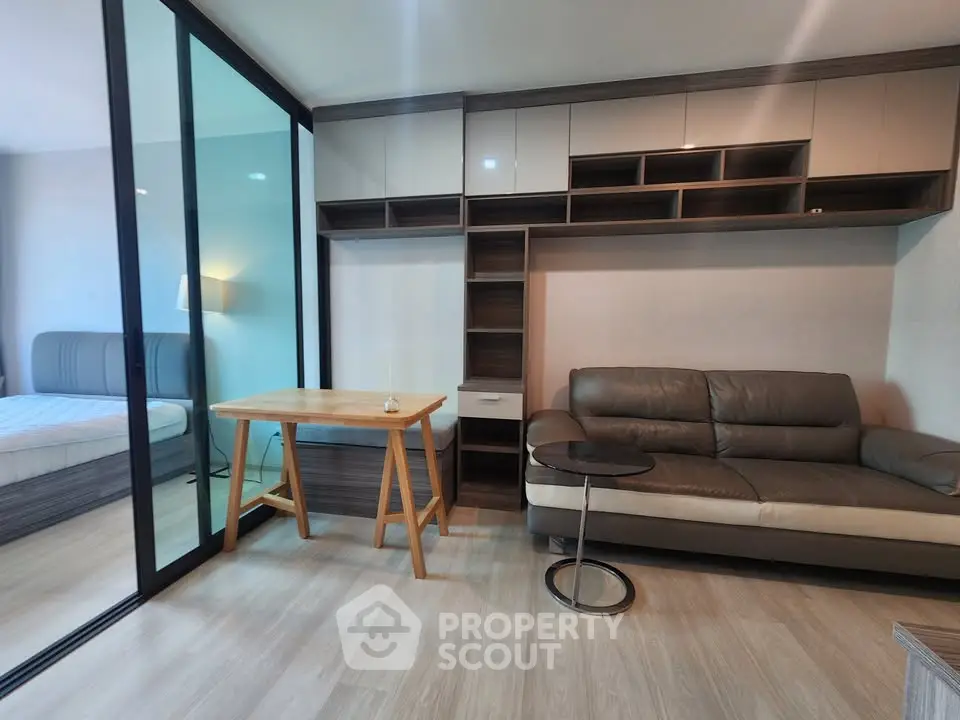 Modern living room with sleek furniture and glass partition leading to bedroom