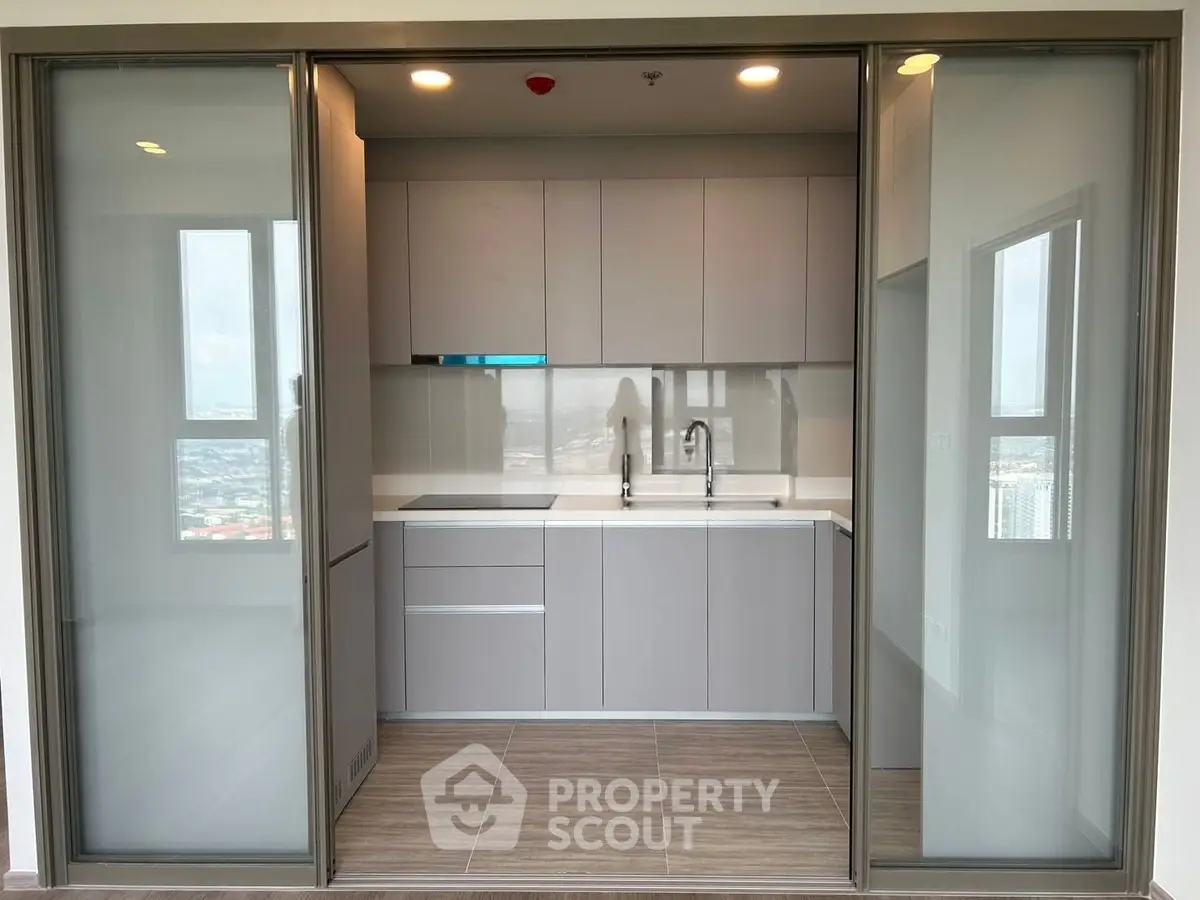 Modern kitchen with sleek cabinetry and sliding glass doors in a high-rise apartment.