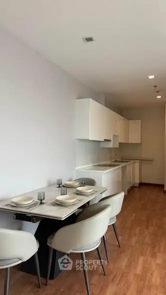 Modern kitchen with sleek white cabinets and dining area, featuring elegant tableware and wooden flooring.