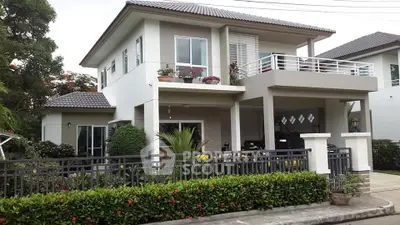 Modern two-story house with balcony and lush garden in a serene neighborhood.