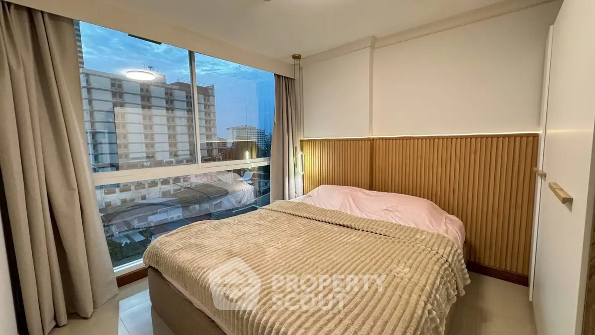 Cozy bedroom with large window offering stunning city view, modern decor, and comfortable bedding.