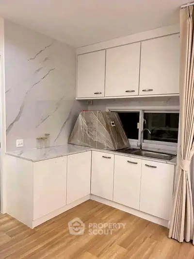 Modern kitchen with sleek white cabinets and marble backsplash in a cozy apartment.