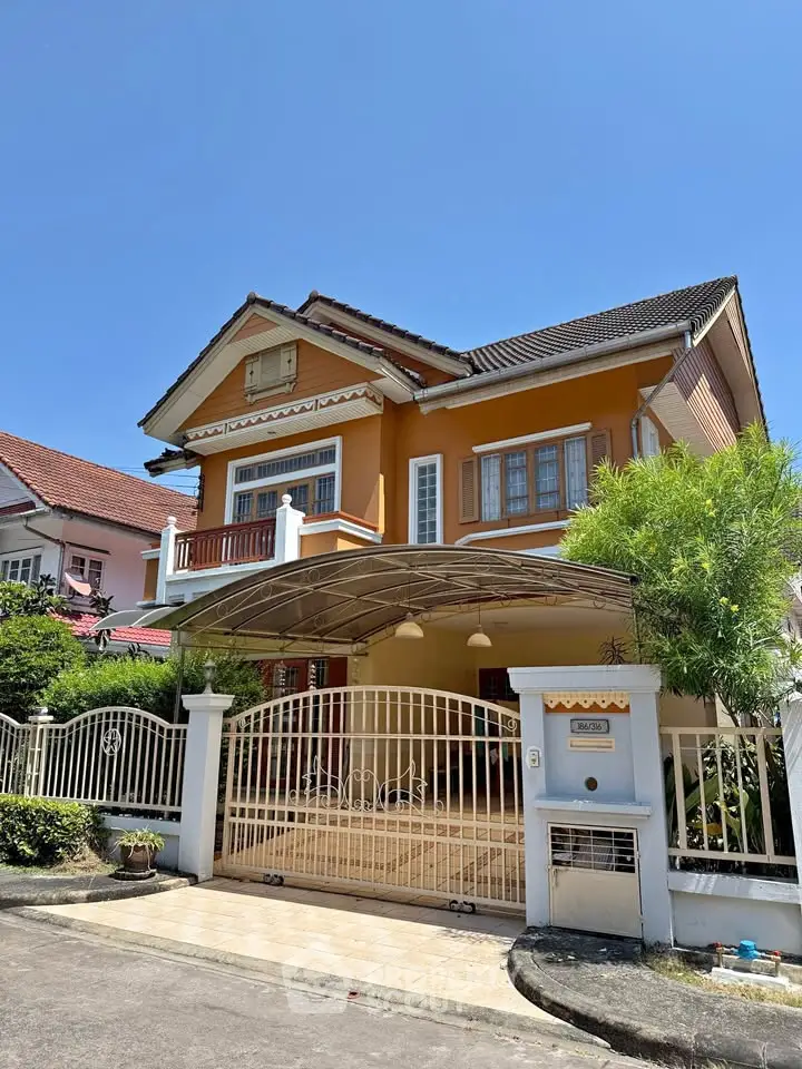 Charming two-story house with gated entrance and lush greenery under a clear blue sky.