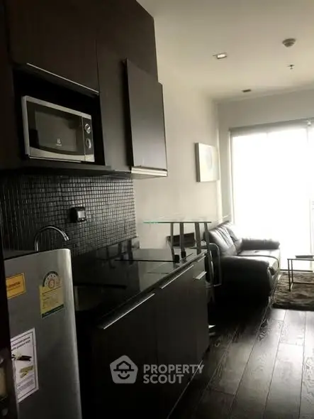 Modern compact living room with kitchenette and sleek dark cabinetry.