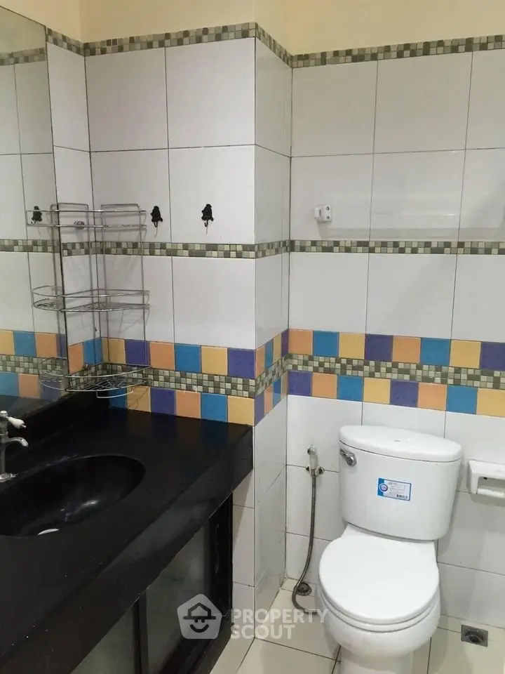 Modern bathroom with colorful tile accents and sleek black countertop.