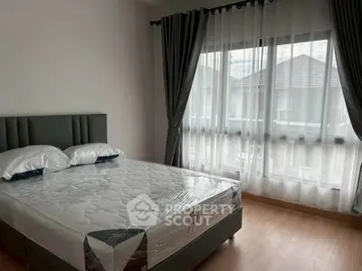Spacious bedroom with large window and modern furnishings in a serene residential setting.