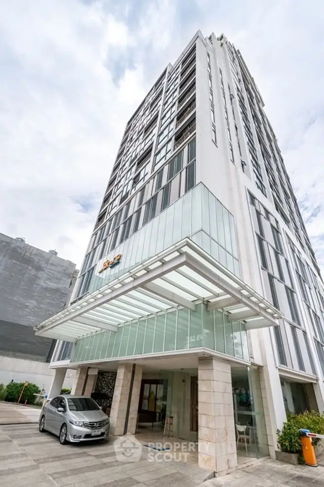 Modern high-rise building with sleek glass facade and covered entrance, ideal for urban living.