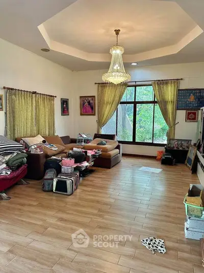 Spacious living room with chandelier and large window, featuring cozy sofas and wooden flooring.