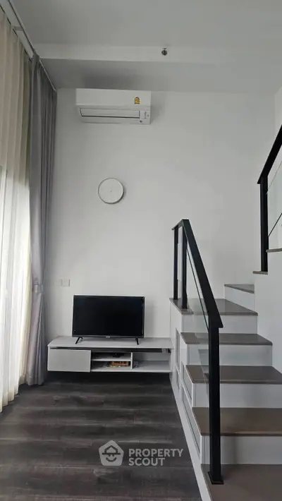 Modern living room with sleek staircase and wall-mounted air conditioner, perfect for urban living.