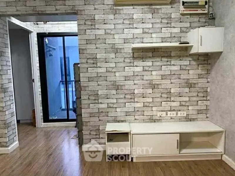Modern living room with stylish brick wall and wooden flooring, featuring sleek white shelving and media unit.