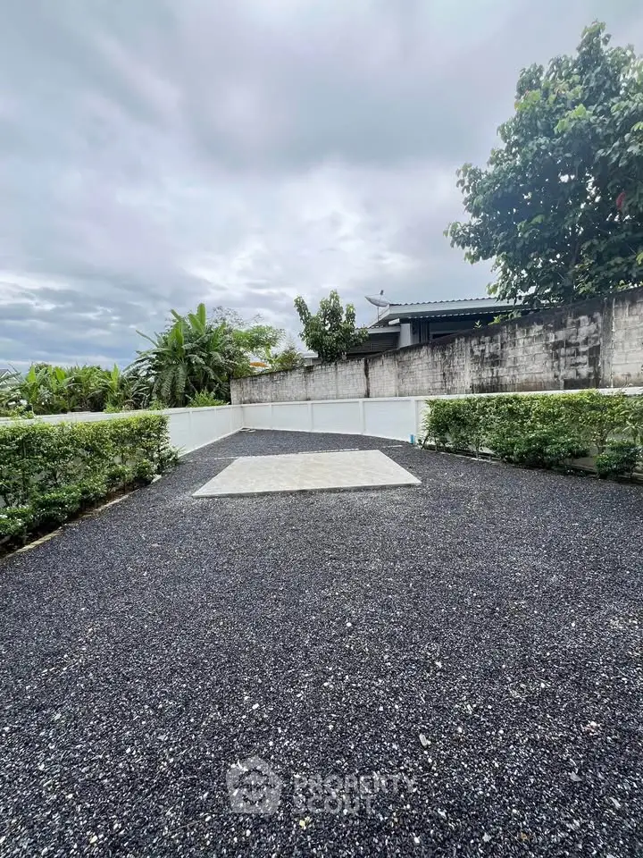 Spacious outdoor area with gravel surface and lush greenery, perfect for landscaping or outdoor activities.