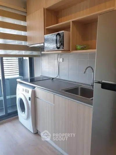 Modern compact kitchen with washing machine and microwave, featuring sleek cabinetry and large window.