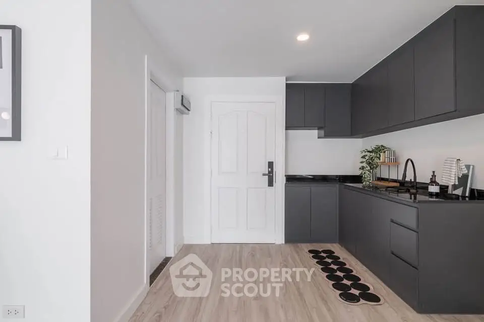 Modern kitchen with sleek black cabinets and light wood flooring in a stylish apartment.