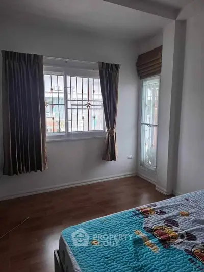 Cozy bedroom with large window and wooden flooring, perfect for natural light lovers.