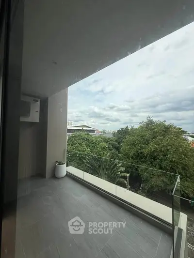 Spacious balcony with glass railing offering lush green views