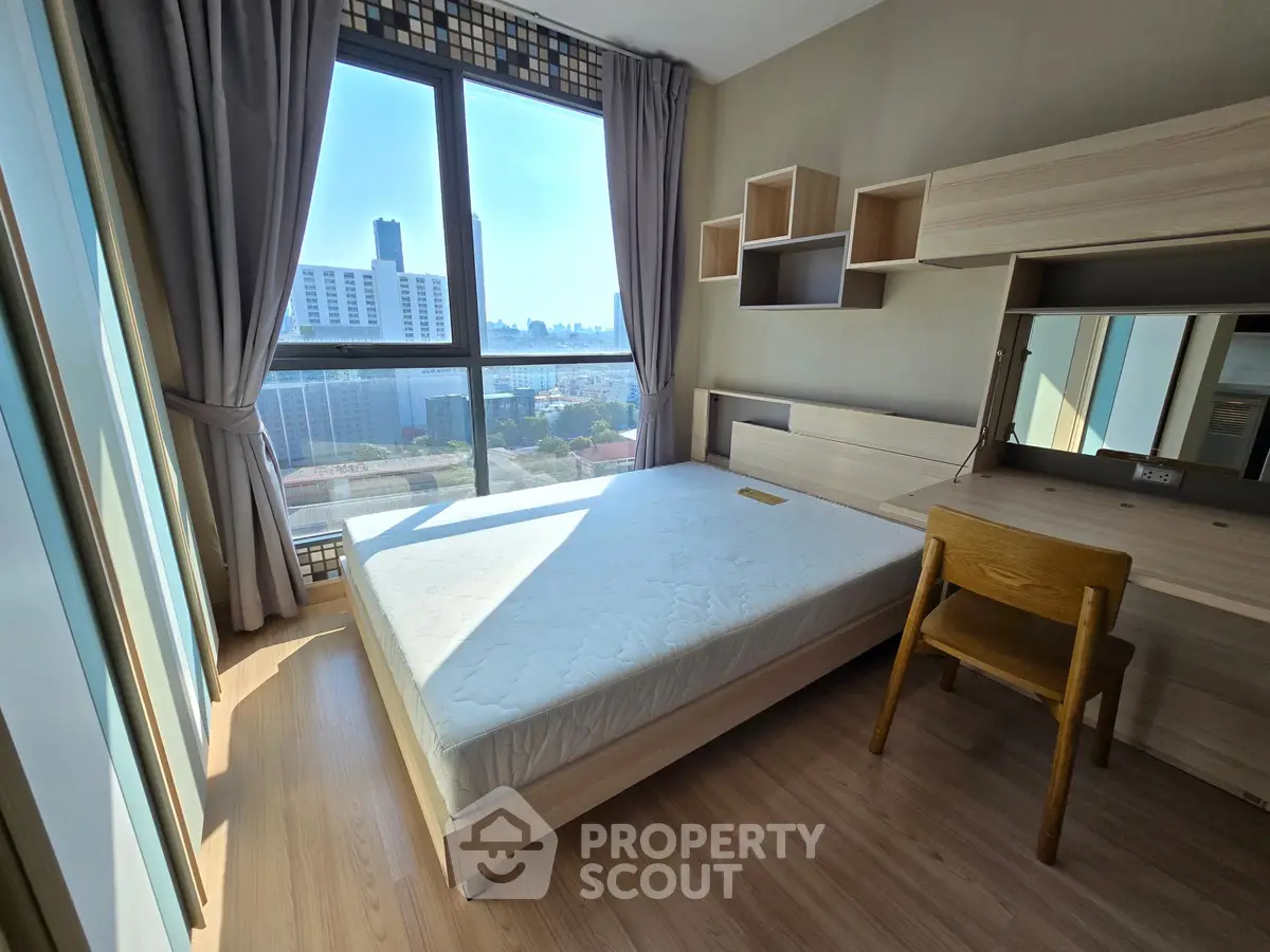 Bright bedroom with large window offering stunning city views, featuring modern furniture and ample natural light.