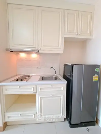 Compact kitchen with white cabinets and stainless steel fridge in modern apartment.