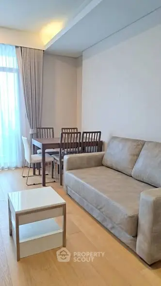 Modern living room with cozy sofa and dining area, featuring elegant wooden flooring and natural light.