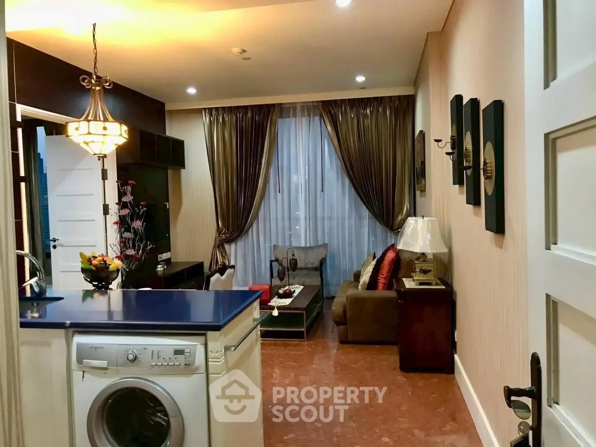 Charming open-layout living room with modern kitchen and cozy decor, featuring a washing machine and elegant lighting.