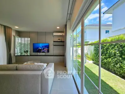 Modern living room with large windows and garden view, featuring sleek furniture and natural light.