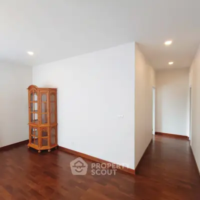 Spacious and well-lit corner unit with polished hardwood floors and a classic wooden display cabinet, perfect for elegant living.