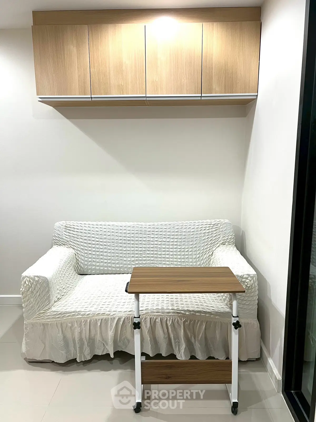 Cozy living room corner with white sofa and wooden cabinet, perfect for compact spaces.