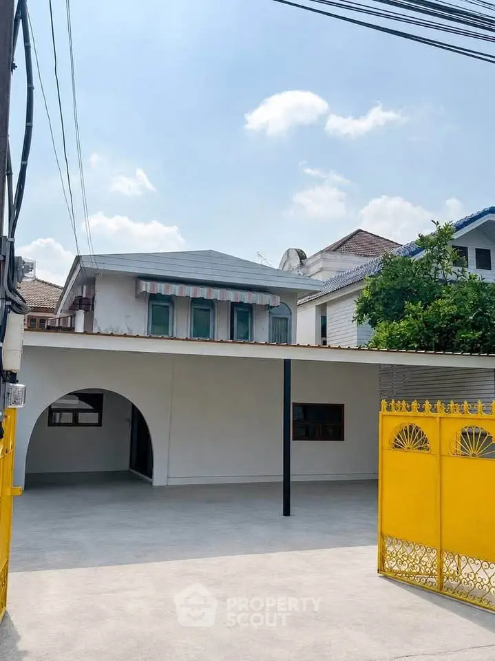 Charming two-story house with spacious courtyard and vibrant yellow gate, perfect for family living.