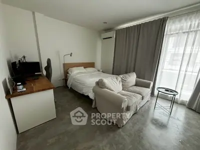 Cozy bedroom with modern decor, featuring a comfortable bed, stylish armchair, and natural light from large windows.