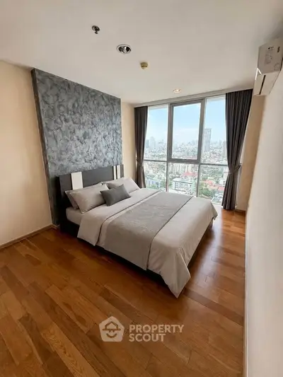 Modern bedroom with city view, featuring wooden flooring and stylish decor in a high-rise apartment.
