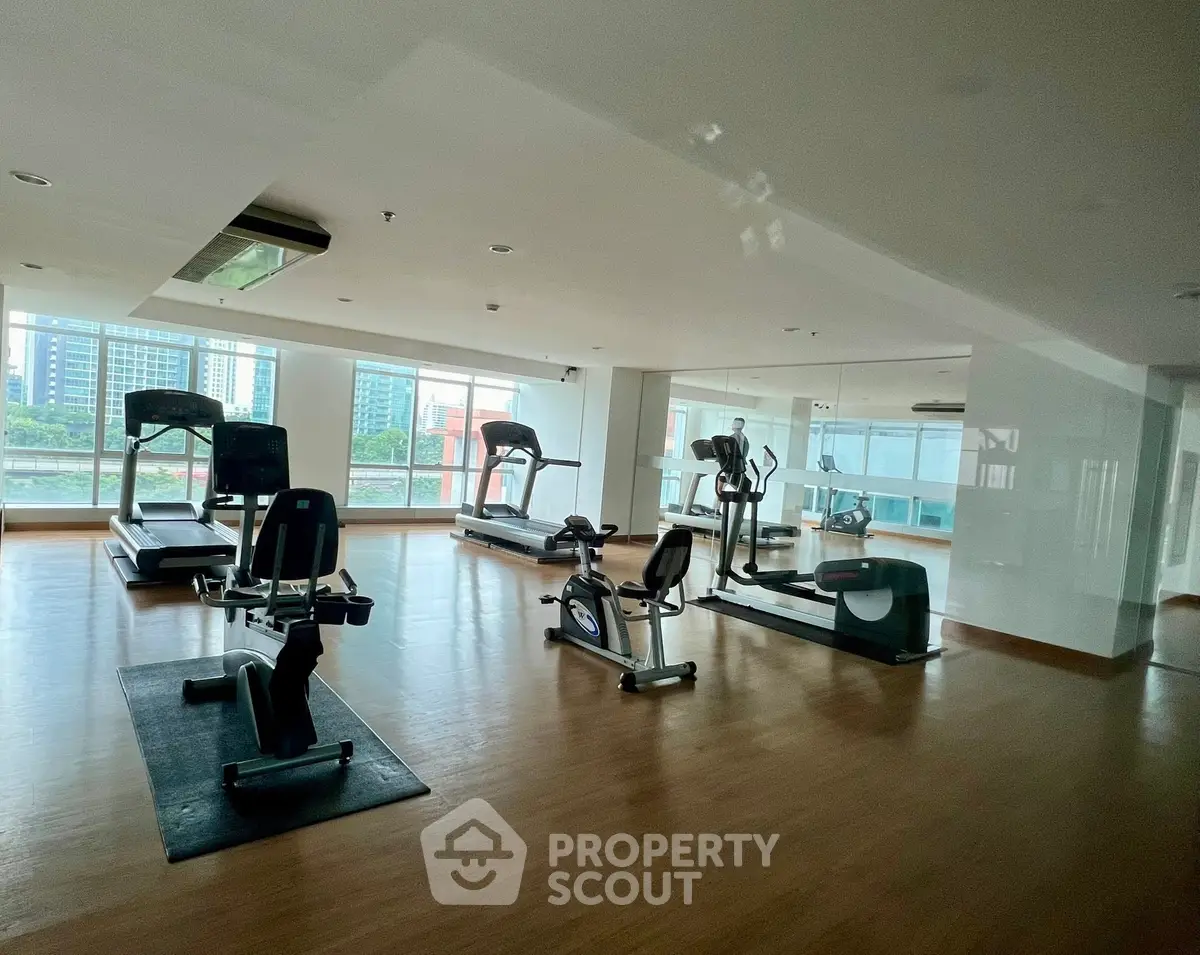 Spacious gym with modern equipment and city view in luxury apartment building.
