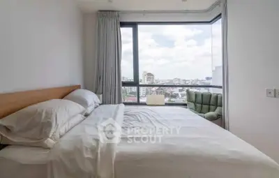 Bright bedroom with large window offering stunning city views and cozy seating area.