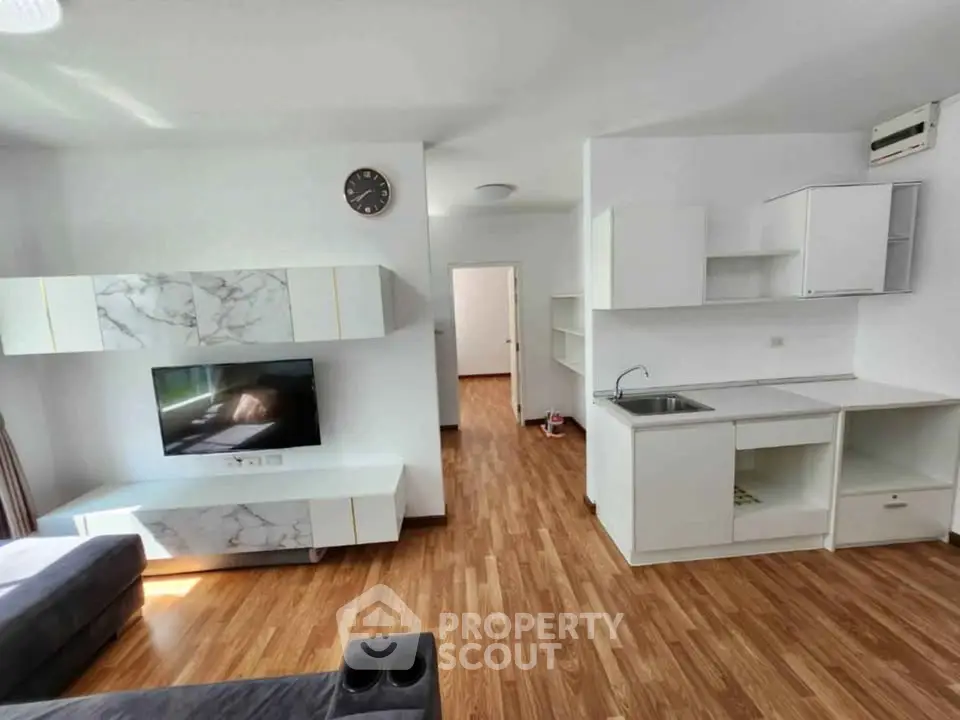 Modern living room with sleek wooden flooring and minimalist white cabinetry.