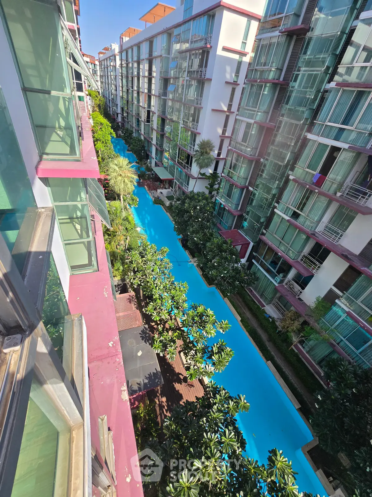 Stunning aerial view of modern apartment complex with lush greenery and a long swimming pool.