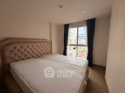 Cozy bedroom with large window offering city view, featuring a plush headboard and elegant curtains.