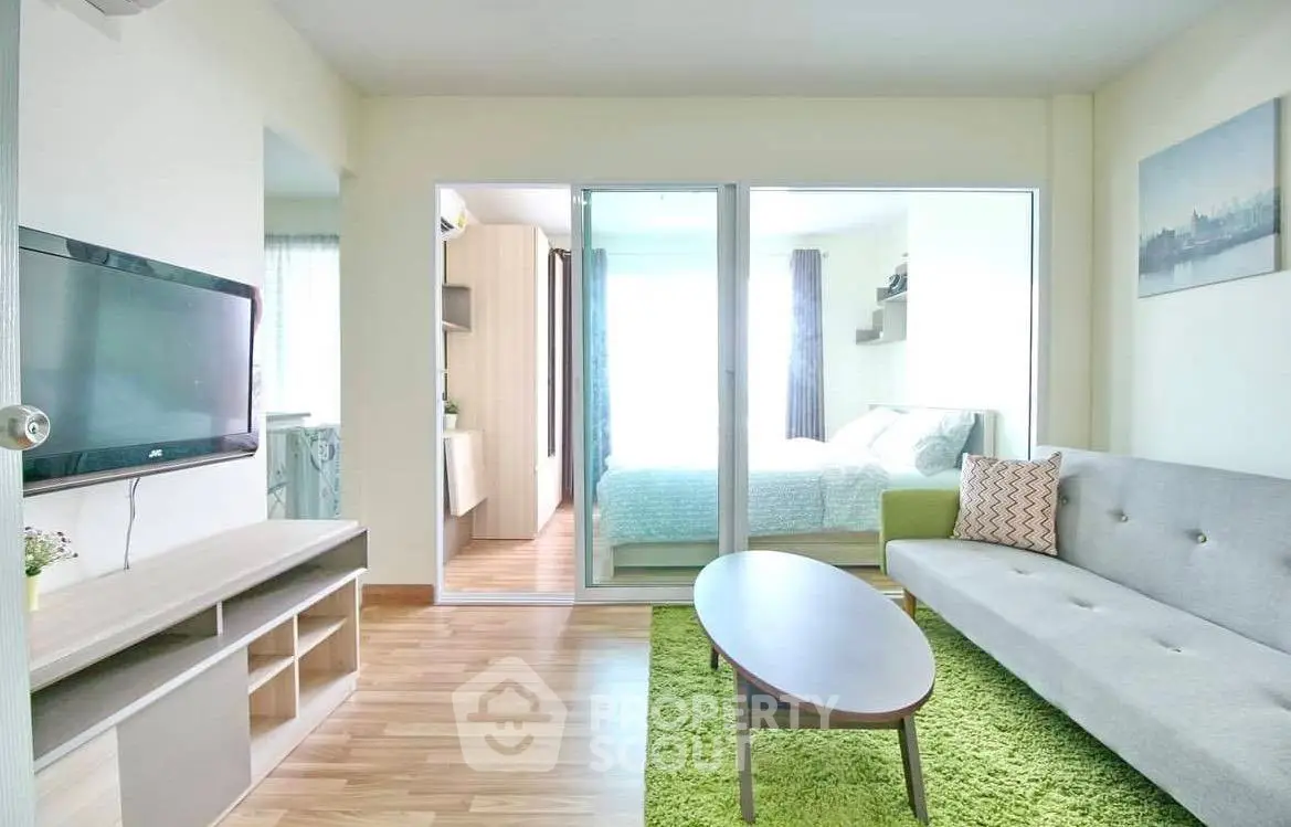Modern living room with sleek furniture and bright decor, featuring a cozy bedroom view through sliding glass doors.