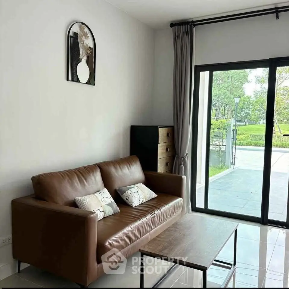 Modern living room with leather sofa and garden view through large glass doors.