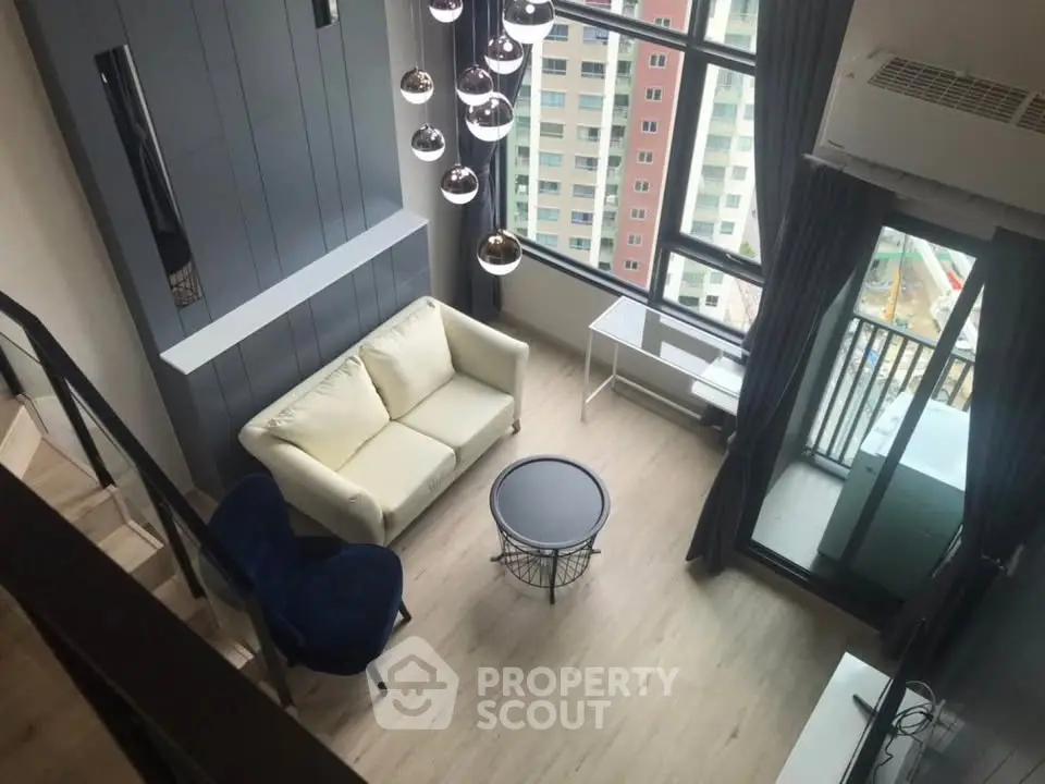 Modern loft-style living room with high ceiling and large windows offering city views.