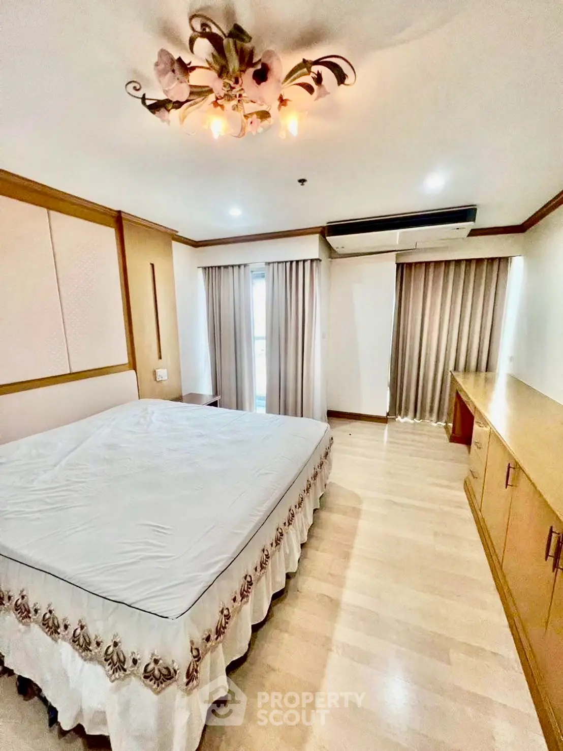Spacious bedroom with elegant chandelier and large windows in modern apartment.