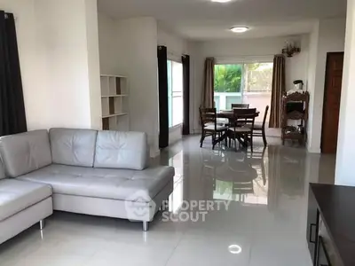 Spacious living room with modern furniture and dining area, featuring large windows and glossy floors.