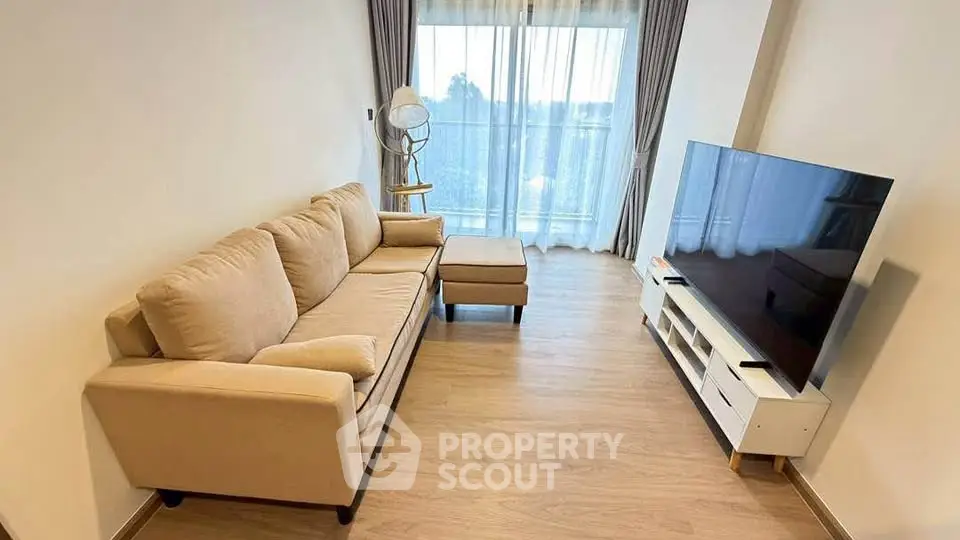 Spacious living room with cozy sofa and large TV, featuring a bright window view.