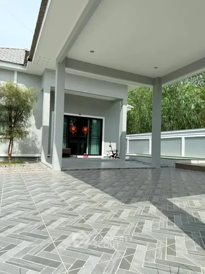 Spacious modern home with elegant tiled patio and lush greenery, perfect for outdoor relaxation.