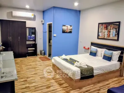 Spacious modern bedroom with stylish decor and wooden flooring, featuring a comfortable bed and air conditioning.